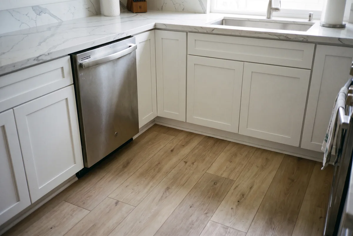 The same kitchen with new vinyl plank flooring laid flat and a new cabinet toe-kick fitted